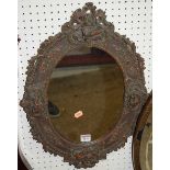 A Continental composite oval framed wall mirror, decorated with winged putti within foliage, 54 x