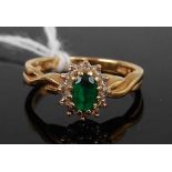 An 18ct gold, emerald and diamond cluster ring, the oval cut emerald in a surround of twelve diamond
