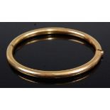 A plain yellow metal hinged bangle, 13.9g, unmarked but tests as approx 14ct, 7cm