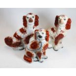 Three various Victorian Staffordshire figures of seated spaniels, having orange sponged