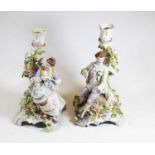 A pair of early 20th century German floral encrusted candlesticks, each surmounted by a seated