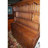 A contemporary joined oak dresser, the panelled back upper section with open shelving, twin cupboard