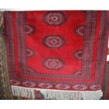 A Persian woollen red ground Bokhara rug having tasselled ends, 185 x 128cm