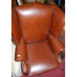 A contemporary tan leather and brass studded wing back scroll armchair, having cushion seat and