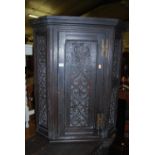A circa 1900 ebonised and floral relief carved oak single door hanging corner cupboard, height 88.
