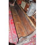 A late Victorian stained oak long church pew raised on shaped faceted end supports with carved