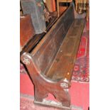 A late Victorian stained oak long church pew, raised on shaped faceted end supports with carved