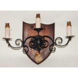 * A mid-20th century wrought iron three sconce wall light fitting on an oak shield shaped plinth,