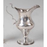 A George III silver pedestal cream jug, of helmet form, having leaf capped double S-scroll handle,
