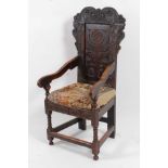 An antique oak Wainscot style chair, having a shaped panelled back with flower head carvings,
