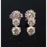 A pair of white metal diamond three-stone drop earrings, each comprising three graduated round