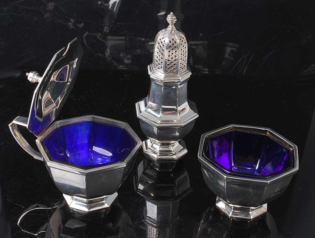 A modern silver three-piece cruet set, comprising open table salt with blue glass liner,