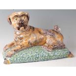 A French faience model of a recumbent pug dog upon a cushion, having all-over sponged decoration (