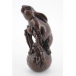 A Japanese carved wooden netsuke modelled as a rabbit tugging on a root vegetable, the rabbit having
