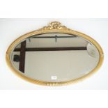 An oval wall mirror with ribbon and reed pattern gilt frame and laurel surmount, 53 x 72 cm