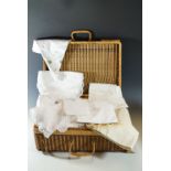 A vintage wicker hamper containing a quantity of vintage linens, including hand embroidered table