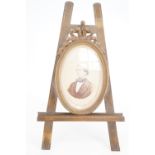 A Victorian brass photograph frame modelled as a ribbon-bow-surmounted oval frame on an easel-form