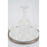 A cut glass liqueur decanter and glasses on mirrored stand, decanter 20 cm