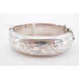 A silver hinged D-section bangle, bearing engraved foliate scroll decoration, Birmingham, 1966