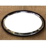 An oval wall mirror, having a bevel-edged plate within a slender ebonized oak frame, circa 1930s, 71