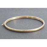A 9ct gold hinged bangle with "feather" engraved edges, 4.4g