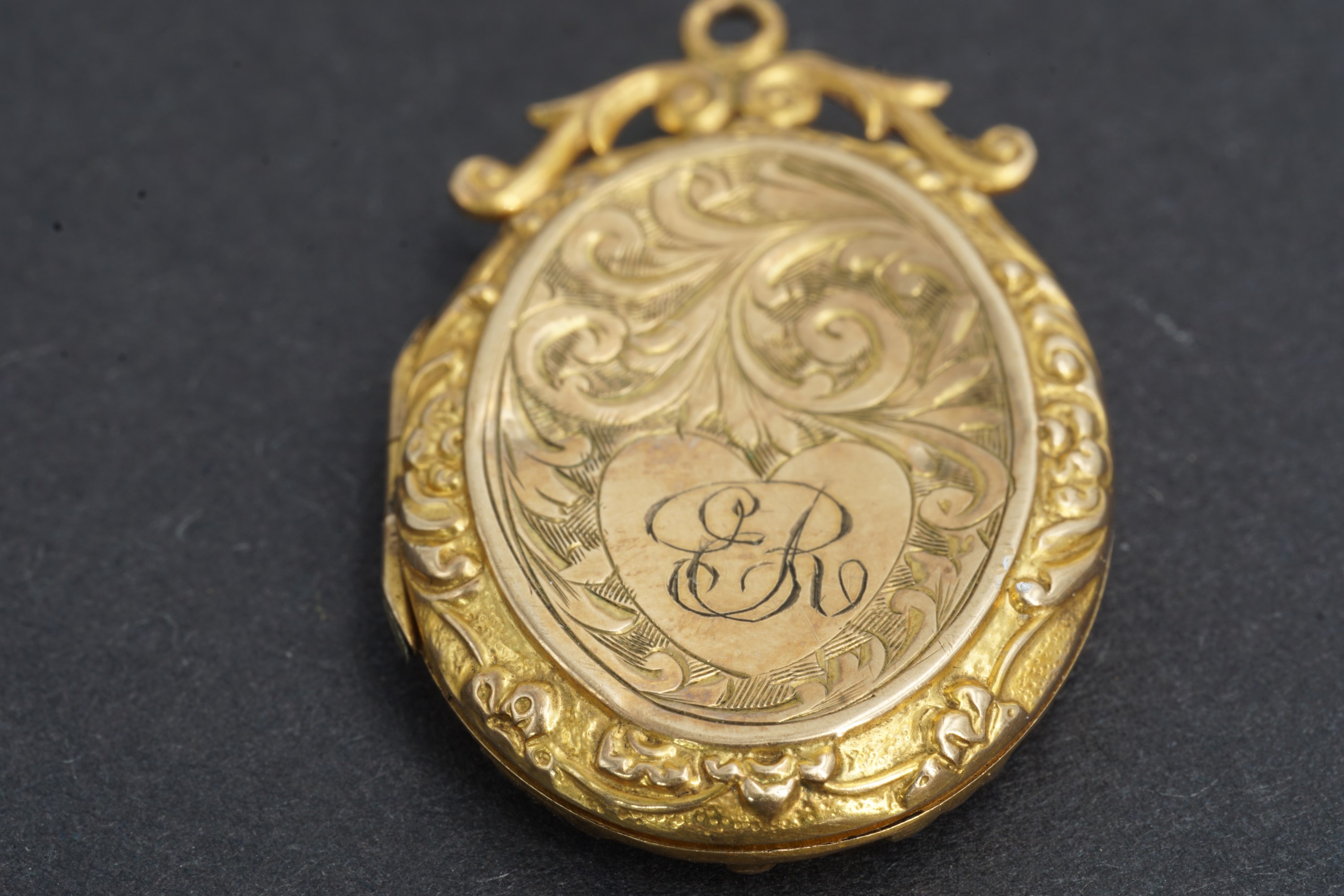 An early 20th Century 9 ct gold pendant locket, foliate-scroll-engraved and having an adorsed scroll