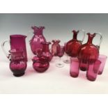 Fourteen items of cranberry glass including two jugs, four vases, two decanters etc.