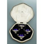 A George V cased set of four silver salts, each having bifurcated scroll handles and cobalt blue