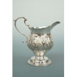 A George III silver footed cream jug, with repousse moulded and chased decoration, surrounding a