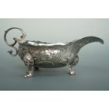 A George III style white metal sauce boat, having three cast feet with masks to the hips and a