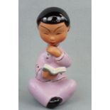 A 1950s - 1960s kitsch painted earthenware figurine of an oriental girl sat reading a book, 20 cm