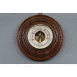 A carved oak barometer by J Dowell and Co, opticians, Maryport and Wigton, 22 cm diameter