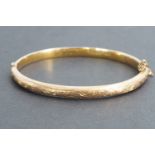 A Victorian 9ct rose gold hinged bangle, the face engraved with scrolling foliage, Chester, 1898, in