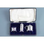 A cased George V silver condiment set, comprising pepper pot, salt cellar and mustard, engraved with