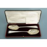 A cased pair of Georgian and later silver berry spoons, with Victorian repousse moulded, chased