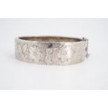 A late Victorian silver hinged bangle, engraved in depiction of blossom and foliage, 6.5 cm x 5 cm