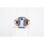 An Art Deco influenced blue stone dress ring, the baguette cut stone set on a yellow metal shank,