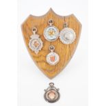 Five vintage silver prize fob medallions presented on an oak shield-shaped display with easel
