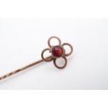 A garnet and yellow metal stick pin, the garnet set within a quatrefoil arrangement of annuli, 0.9