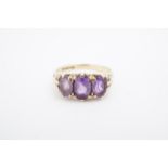 A three-stone amethyst dress ring, the three oval stones scroll-set on a 9 ct gold shank, M