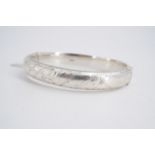 An early 1960s silver hinged bangle, of D-section and engraved in a pattern of spiral bands and