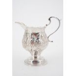 A George III silver footed cream jug, with repousse moulded and chased decoration, surrounding a