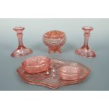 A group of pink pressed glass comprising a tray, two covered dressing table boxes, a pair of