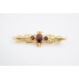 A 9 ct gold and red stone brooch, comprising three stones set within scrolls between anthemions, 4