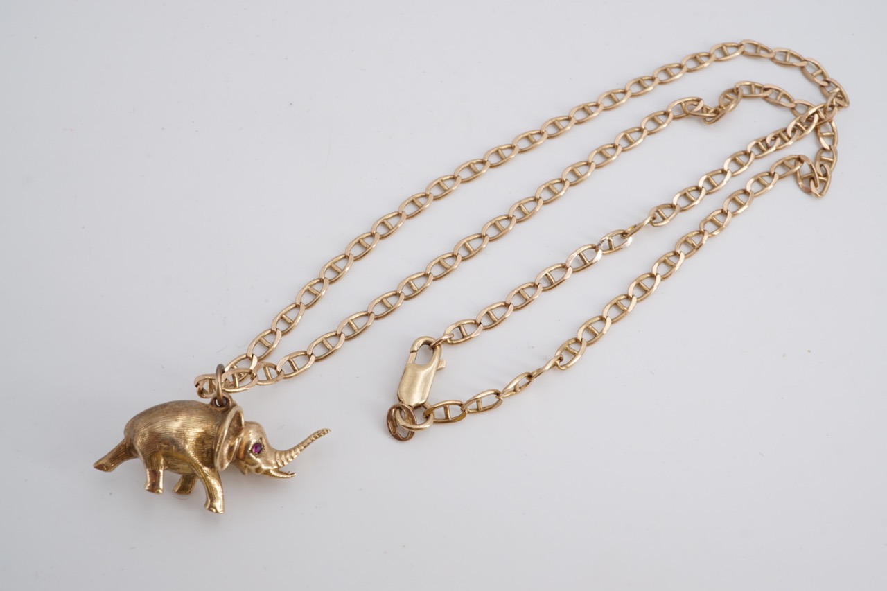 A yellow metal pendant modelled as an elephant, having ruby eyes, on a 9 ct gold marine link neck