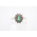 An emerald and diamond flowerhead cluster ring, the central oval-cut emerald 5 x 3 mm, having a 9 ct