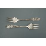 A pair of Edwardian silver pickle forks, their terminals fretted and engraved in depiction of
