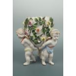 A late 19th Century porcelain figural vase, the rose-encrusted oviform vase held aloft by three