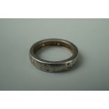 A precious white metal wedding band, pierced and engraved in a pattern on scrolls divided by