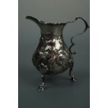 A Georgian silver baluster cream jug, repousse-worked and engraved in a floral pattern centred by